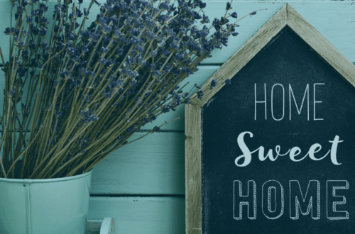 Sign that read home sweet home resting against a wooden wall with a pot of purple flowers next to it